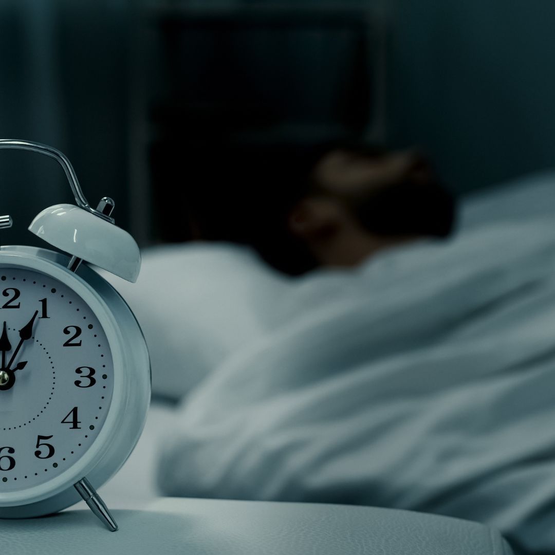 Alarm clock with blurry person sleeping in the background.