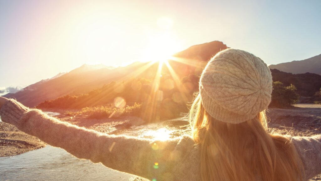 Woman facing a vibrant mountain sunrise with open arms.