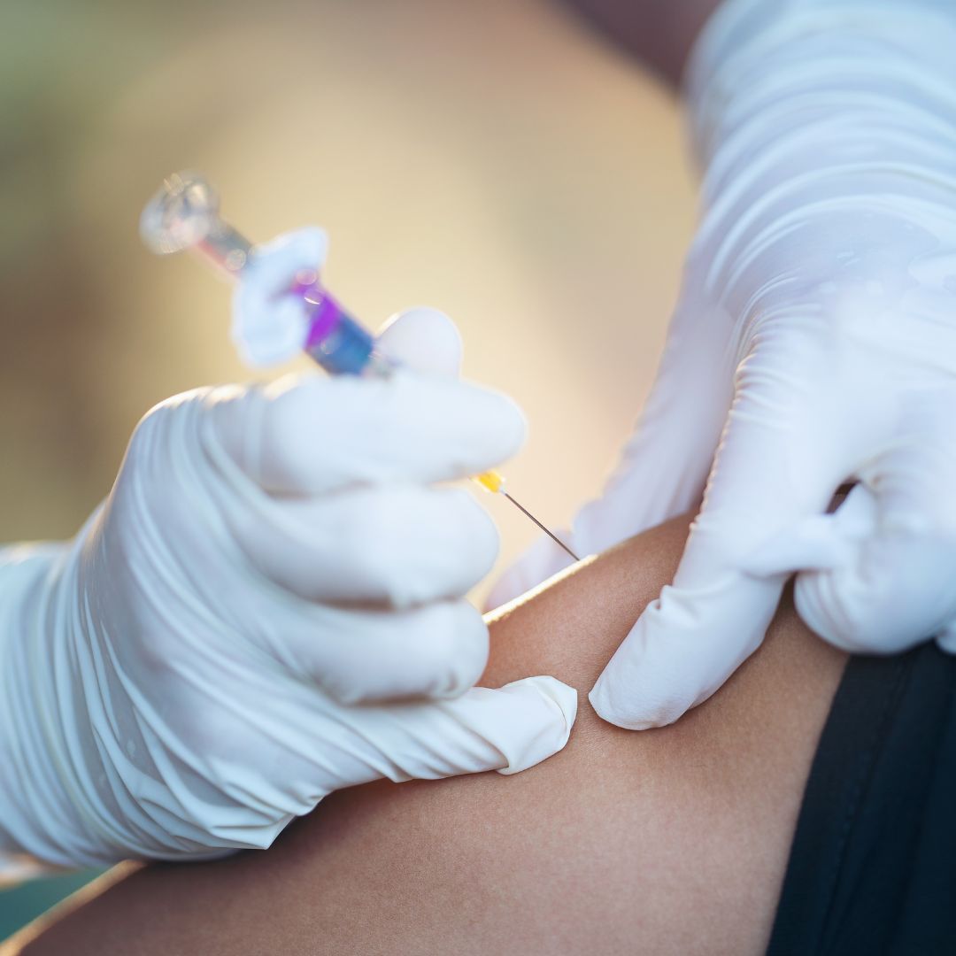 Gloved hands giving a patient an injection.