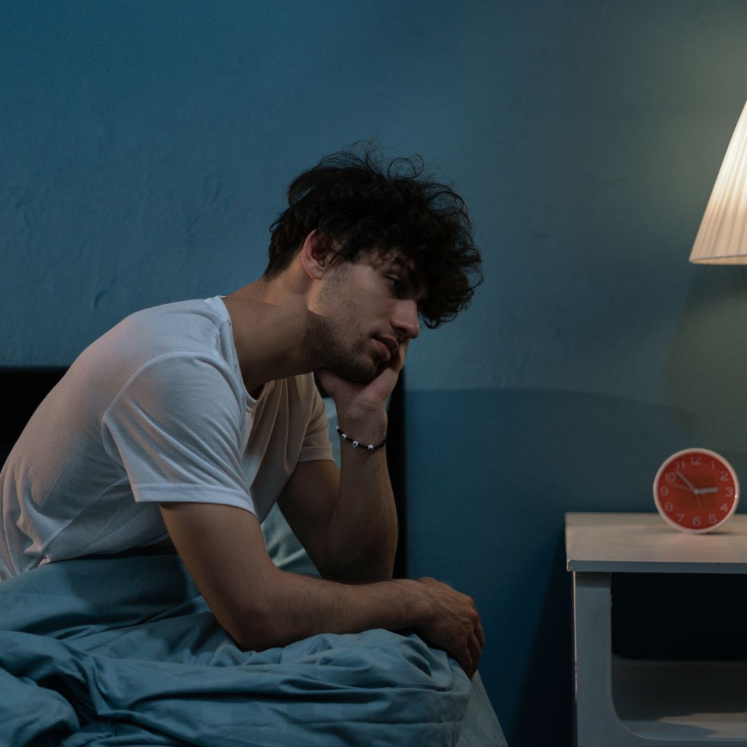 Exhausted man sitting on bed at night.