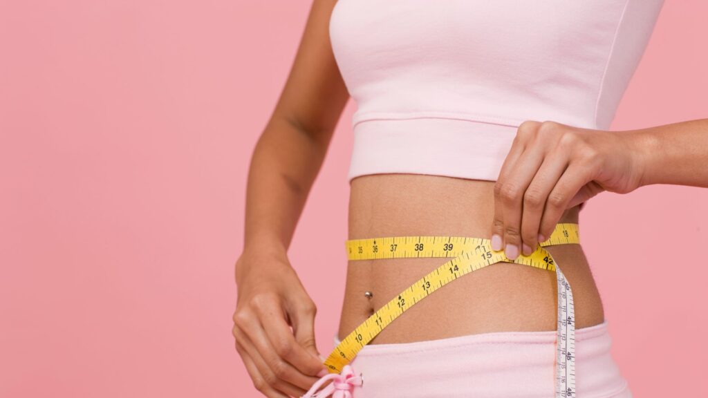 Woman measuring her waist with yellow tape measure.