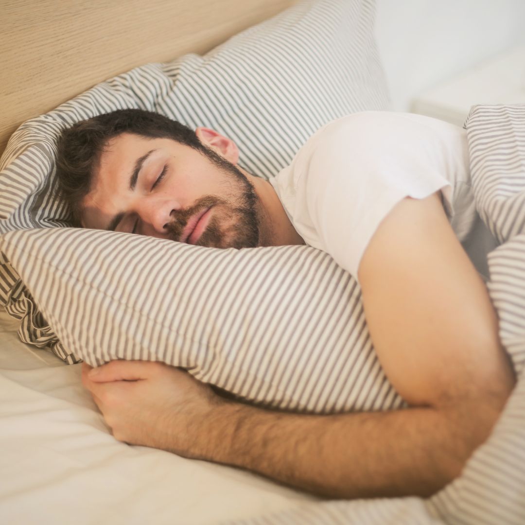 Man sleeping peacefully in bed with striped bedding.