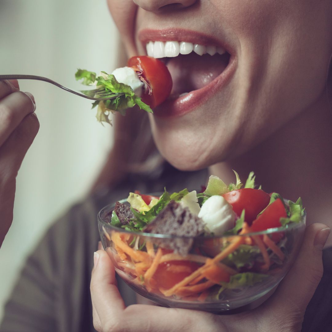 Close-up of a smiling woman eating a salad.