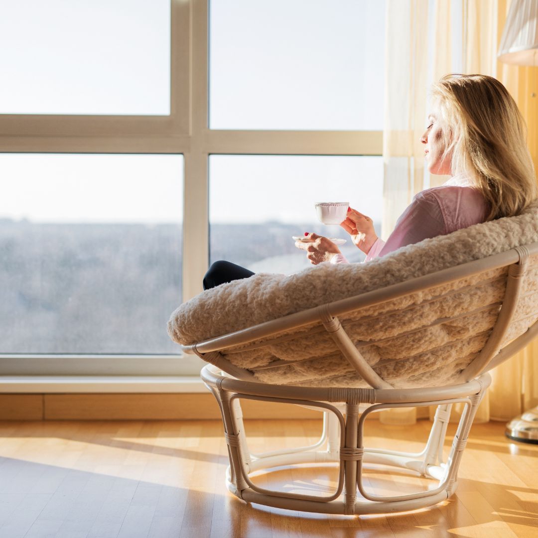 Woman relaxing in chair by window drinking tea.