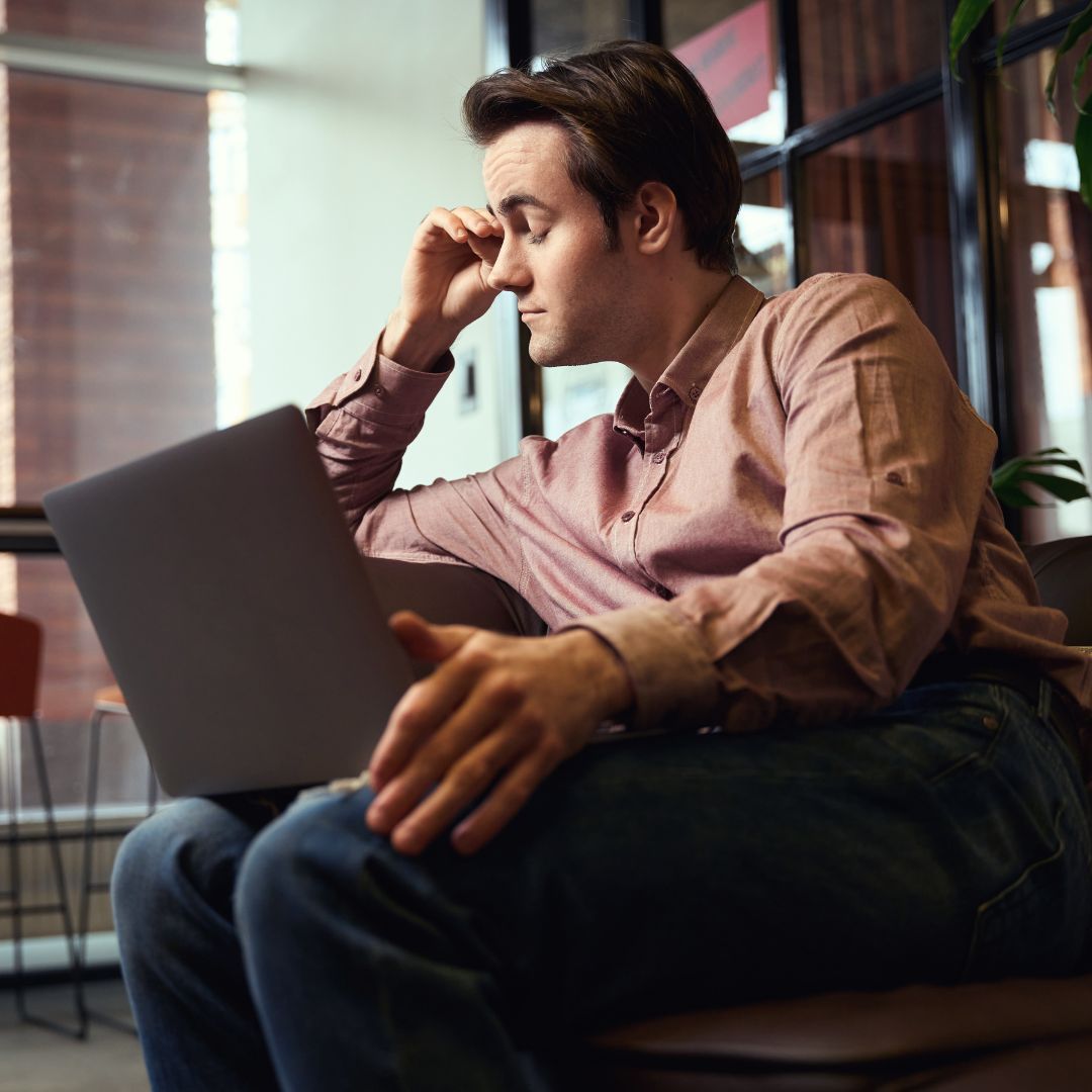 Fatigued man rubbing his eyes at a laptop.