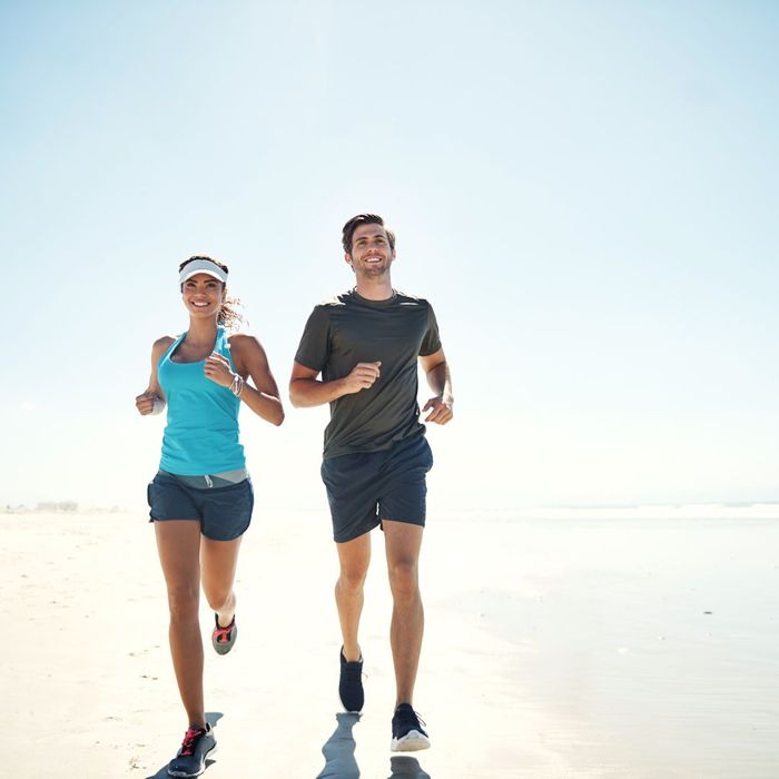 Man and woman jogging together on a sunny beach.